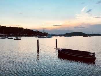 Sailboats moored on sea against sky during sunset