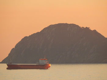 Boat sailing on sea against orange sky