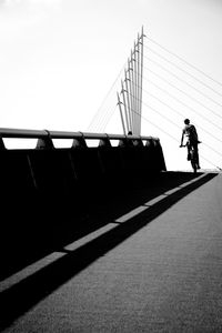 Rear view of man cycling on footbridge on road