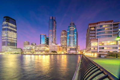 Illuminated buildings by river against sky in city at night