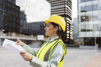 Engineer wearing hardhat holding blueprint working outside modern building