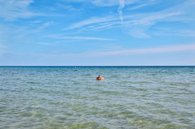 Mid distance view of girl with inflatable ring floating on sea against sky