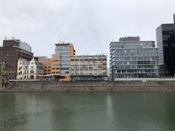 Buildings by river against sky in city