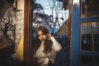 Portrait of young woman looking through window