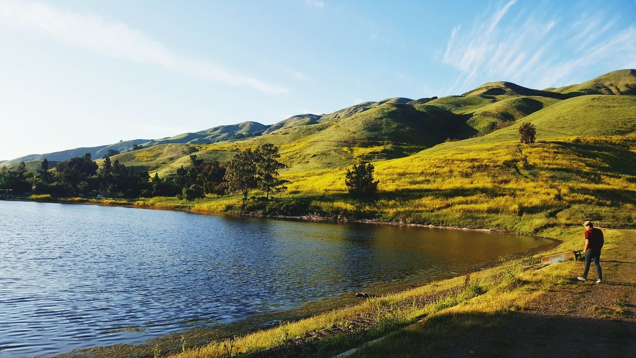 nature, beauty in nature, tranquil scene, scenics, sky, real people, day, lake, non-urban scene, mountain, tranquility, water, outdoors, landscape, grass, lifestyles, one person, full length, tree, people