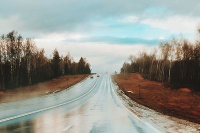 Empty road along trees and plants against sky