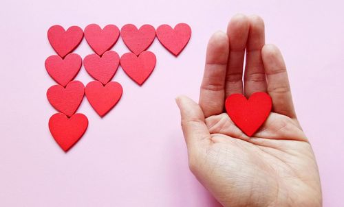 Close-up of person hand holding heart shape over pink background