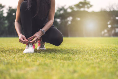 Low section of woman tying shoelace on grassy land