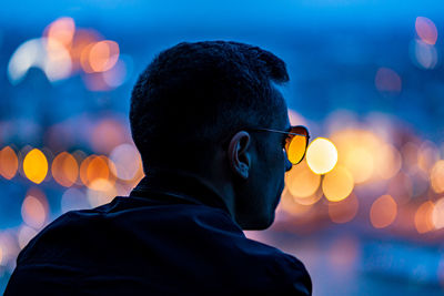 Rear view of man in sunglasses outdoors at dusk