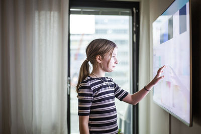 Side view of woman looking through window at home