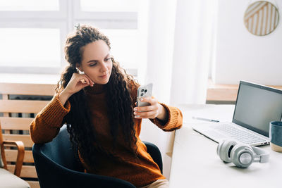 Portrait of young woman using mobile phone while sitting at home