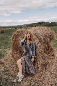 Full length of young woman on hay bales in field