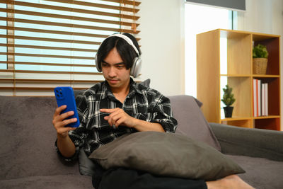 Young woman using mobile phone while sitting on sofa at home