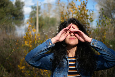 Young woman rubbing eyes while standing against trees in forest