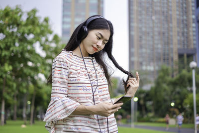 Young woman listening music while standing in park