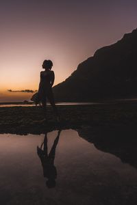 Silhouette woman standing at beach against clear sky during sunset