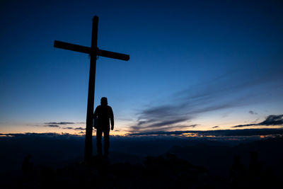 Silhouette men standing by cross against sky during sunset