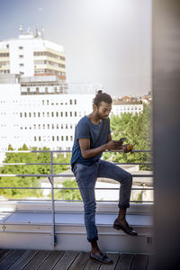 Side view of young man standing against buildings in city