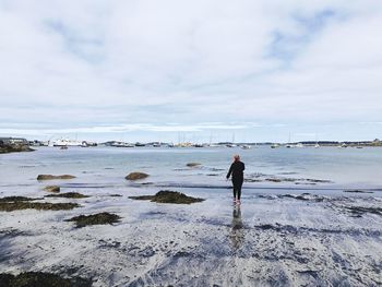 Rear view of woman walking at beach against sky