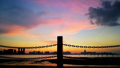 Silhouette bridge over sea against dramatic sky during sunset