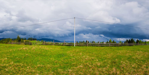 Electric power transmission pole in the mountains with cables along a wooden rail fence