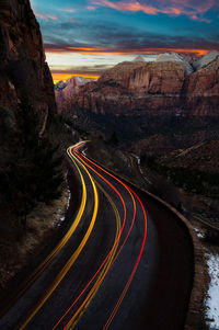 Light trails on road by rock formation against sky