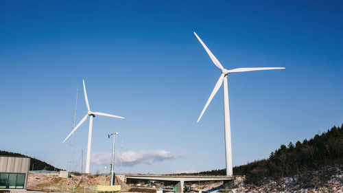 Low angle view of wind turbines on field against clear blue sky