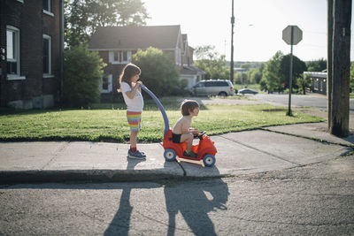 Siblings playing with toy car on footpath against sky