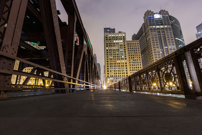 Illuminated road amidst buildings against sky at night