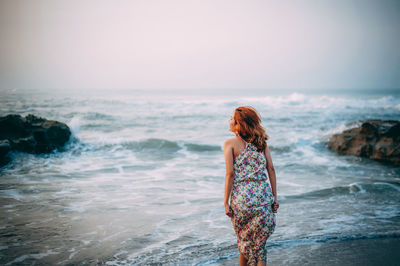 Rear view of woman standing on shore against sky