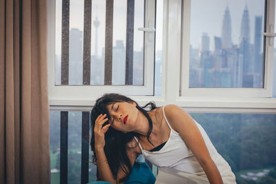 Young woman looking through window at home