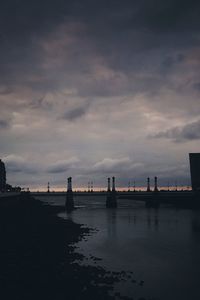 Silhouette lighthouse by sea against sky during sunset