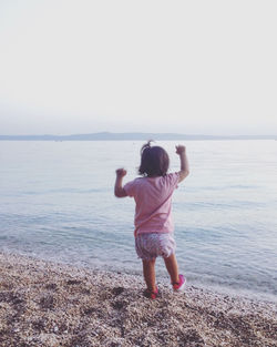 Baby girl playing at sea shore against clear sky