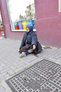 Man sitting on sidewalk in city