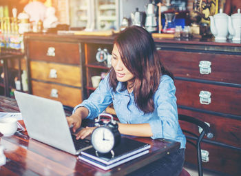 Young woman using phone while sitting on laptop