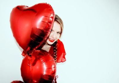 Portrait of happy woman with heart shape balloons against white background