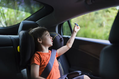 Cute boy playing with toy rocket on back seat of car