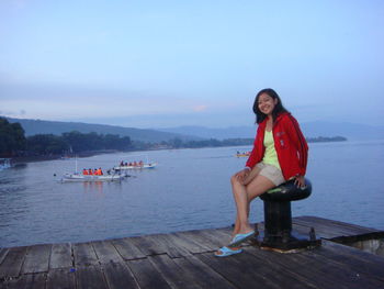 Portrait of young woman sitting on pier over lake