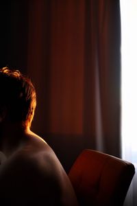 Side view of shirtless man sitting on chair at home