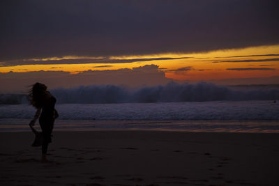 Rear view of silhouette man standing on beach against sky at sunset