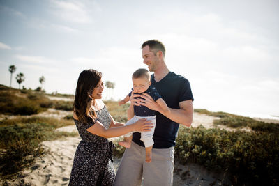 Mother & father smiling & holding infant son on beach