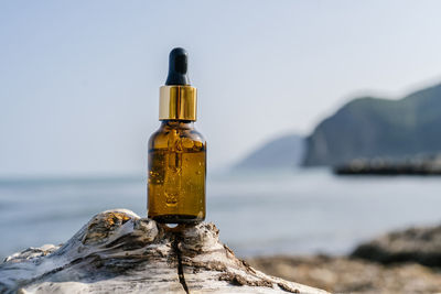 Close-up of bottle on rock by sea against clear sky