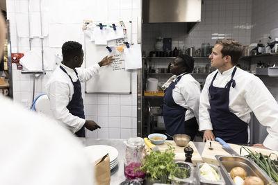 Male chef explaining to colleagues over whiteboard in kitchen of restaurant