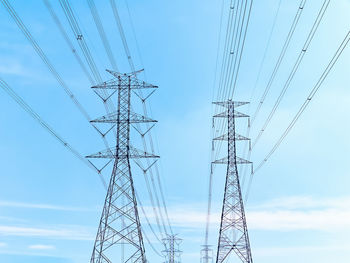 Low angle view of high voltage electrical transmission towers and cables against blue sky
