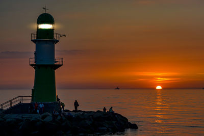 Lighthouse by sea against sky during sunset