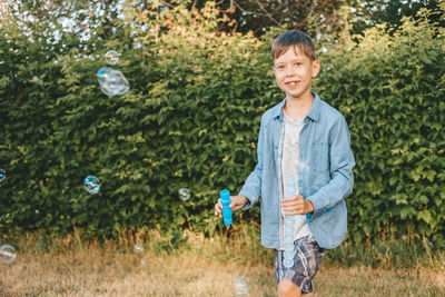 A boy is playing with soap bubbles in a summer park, among the greenery.