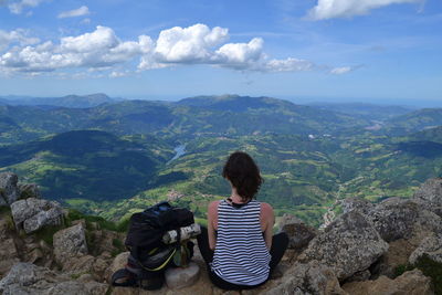 Rear view of woman sitting on rock against sky