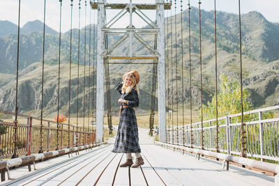 Happy young blonde woman in plaid dress on horochowski bridge on katun river, altai mountains
