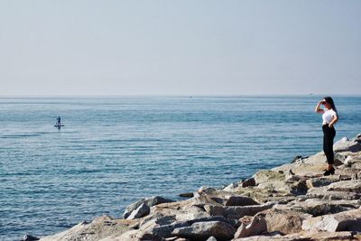 Woman standing on rock by sea against clear sky