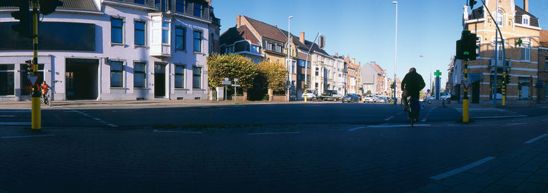 Panoramic city street with a bicyclist waits at city crossroad by traffic light